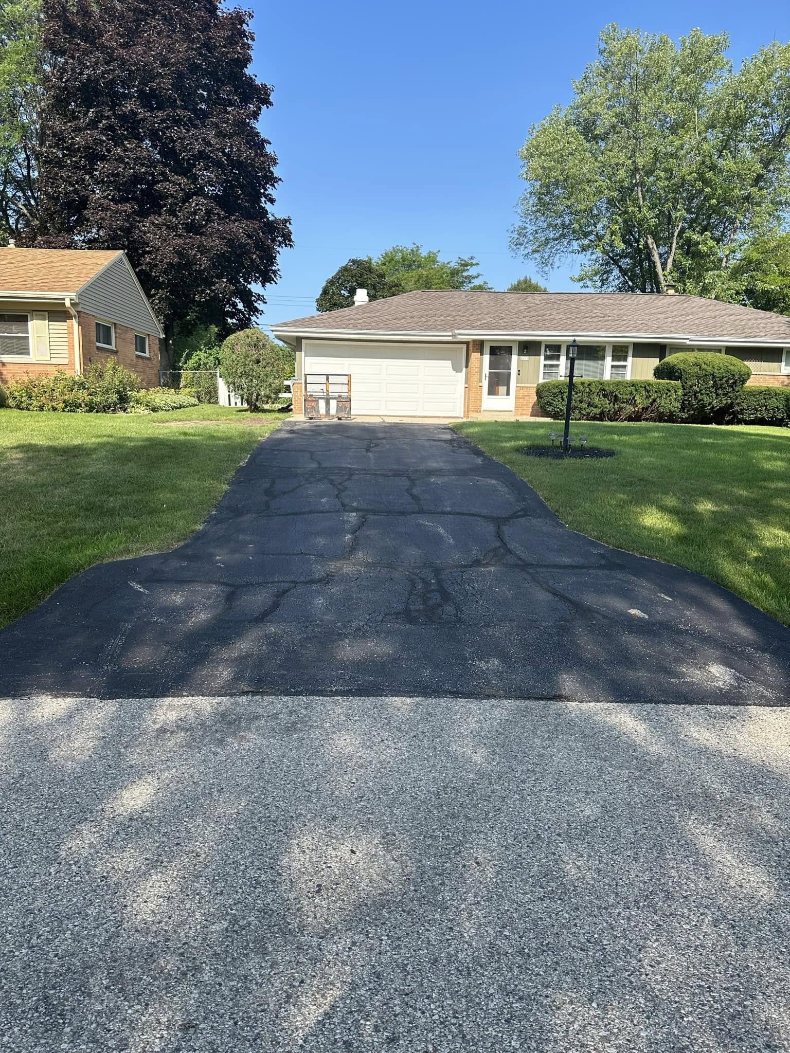 Existing cracked and patched asphalt driveway leading to detached garage showing before condition